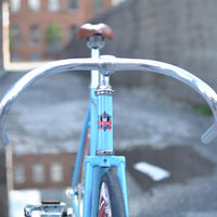 This fixed gear bicycle is called "The Maquis" and features red rims and a sky blue frame.