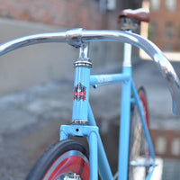 This fixed gear bicycle is called "The Maquis" and features red rims and a sky blue frame.