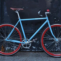 This fixed gear bicycle is called "The Maquis" and features red rims and a sky blue frame.