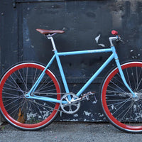 This fixed gear bicycle is called "The Maquis" and features red rims and a sky blue frame.
