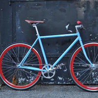 This fixed gear bicycle is called "The Maquis" and features red rims and a sky blue frame.