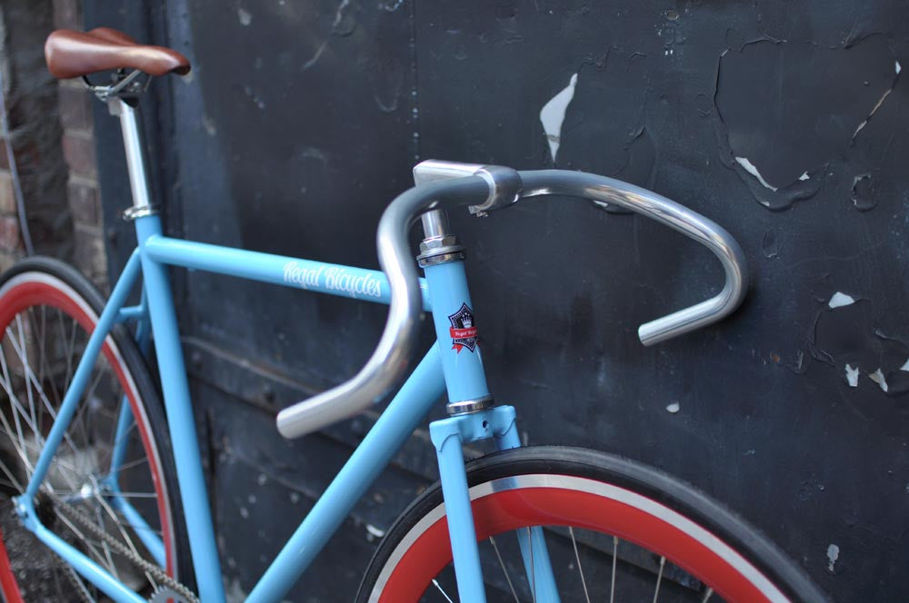 This fixed gear bicycle is called "The Maquis" and features red rims and a sky blue frame.