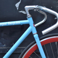 This fixed gear bicycle is called "The Maquis" and features red rims and a sky blue frame.