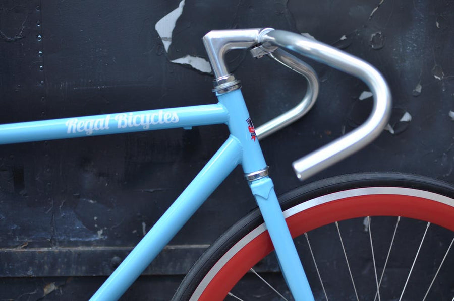 This fixed gear bicycle is called "The Maquis" and features red rims and a sky blue frame.