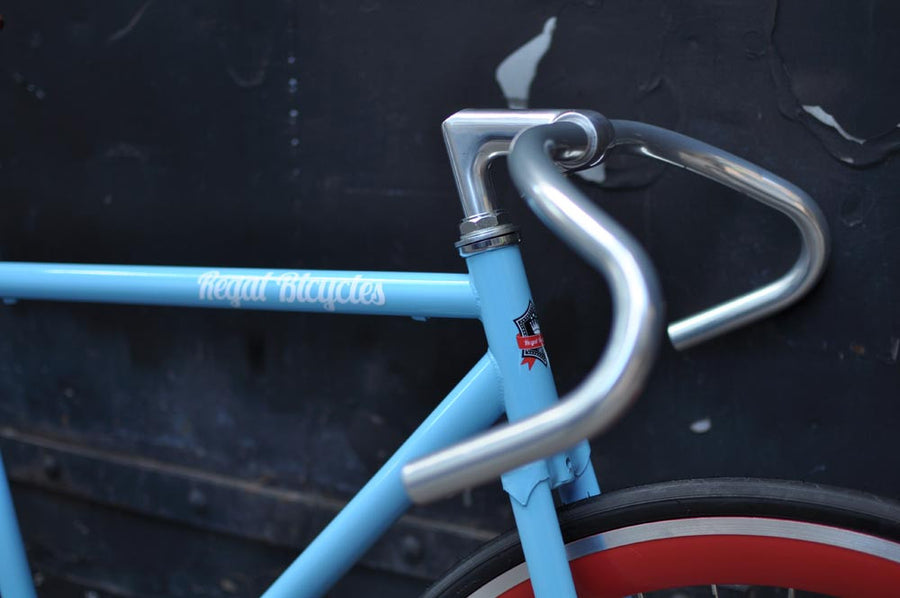 This fixed gear bicycle is called "The Maquis" and features red rims and a sky blue frame.