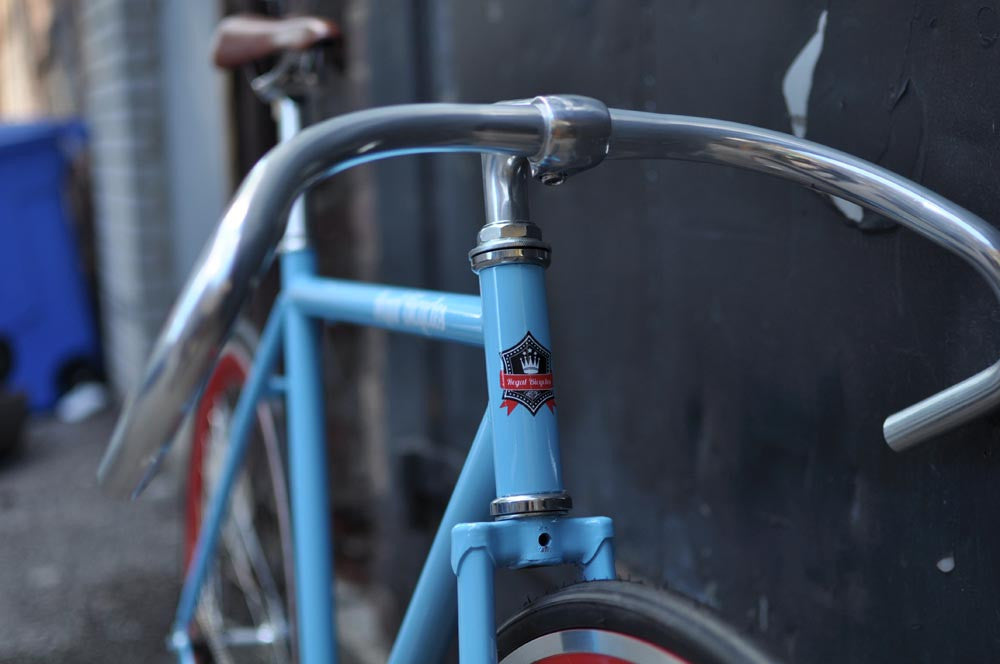 This fixed gear bicycle is called "The Maquis" and features red rims and a sky blue frame.