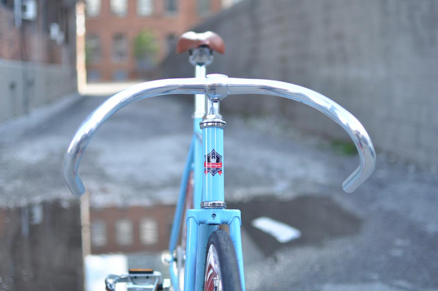 This fixed gear bicycle is called "The Maquis" and features red rims and a sky blue frame.