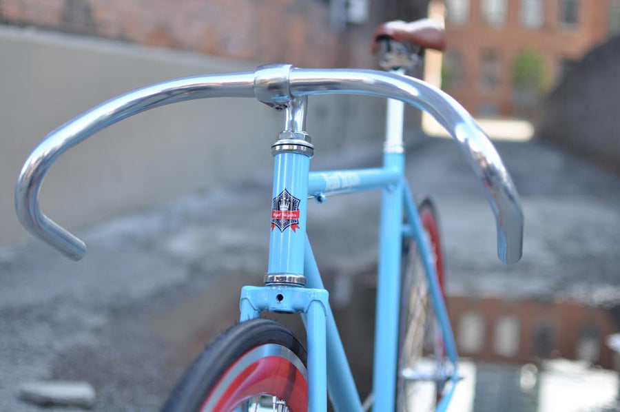 This fixed gear bicycle is called "The Maquis" and features red rims and a sky blue frame.