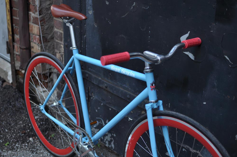 This fixed gear bicycle is called "The Maquis" and features red rims and a sky blue frame.