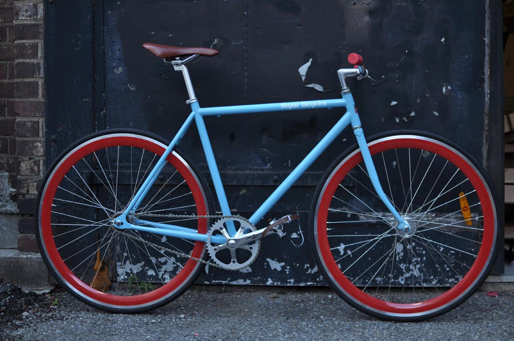 This fixed gear bicycle is called "The Maquis" and features red rims and a sky blue frame.