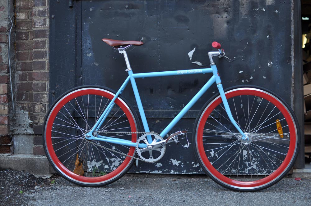 This fixed gear bicycle is called "The Maquis" and features red rims and a sky blue frame.