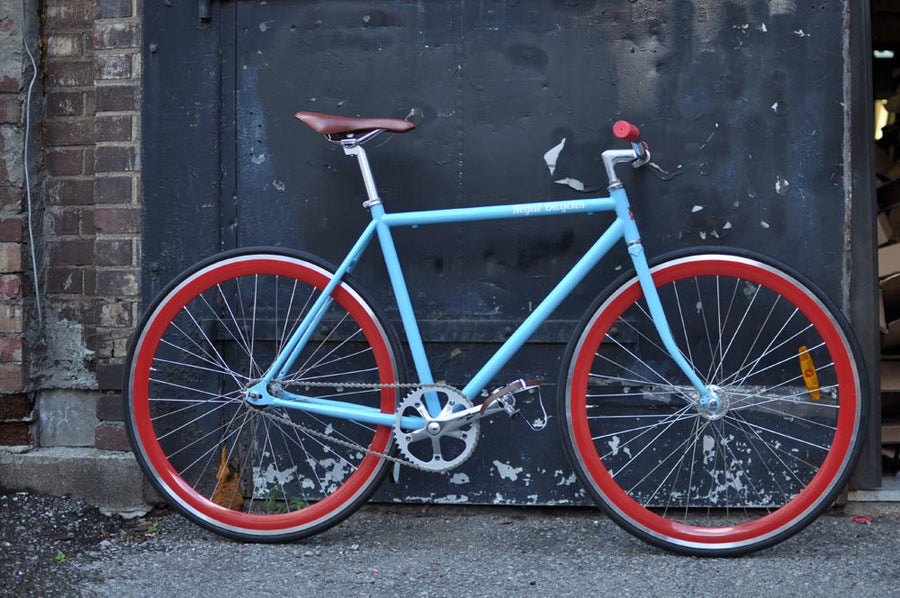 This fixed gear bicycle is called "The Maquis" and features red rims and a sky blue frame.