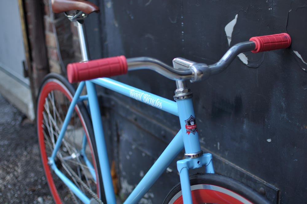 This fixed gear bicycle is called "The Maquis" and features red rims and a sky blue frame.