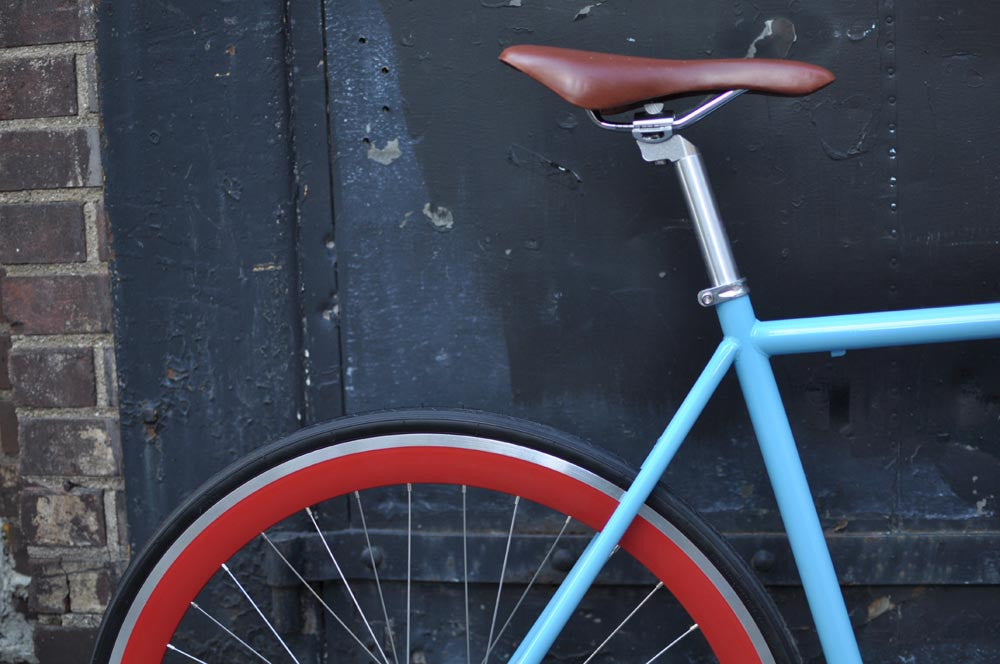 This fixed gear bicycle is called "The Maquis" and features red rims and a sky blue frame.