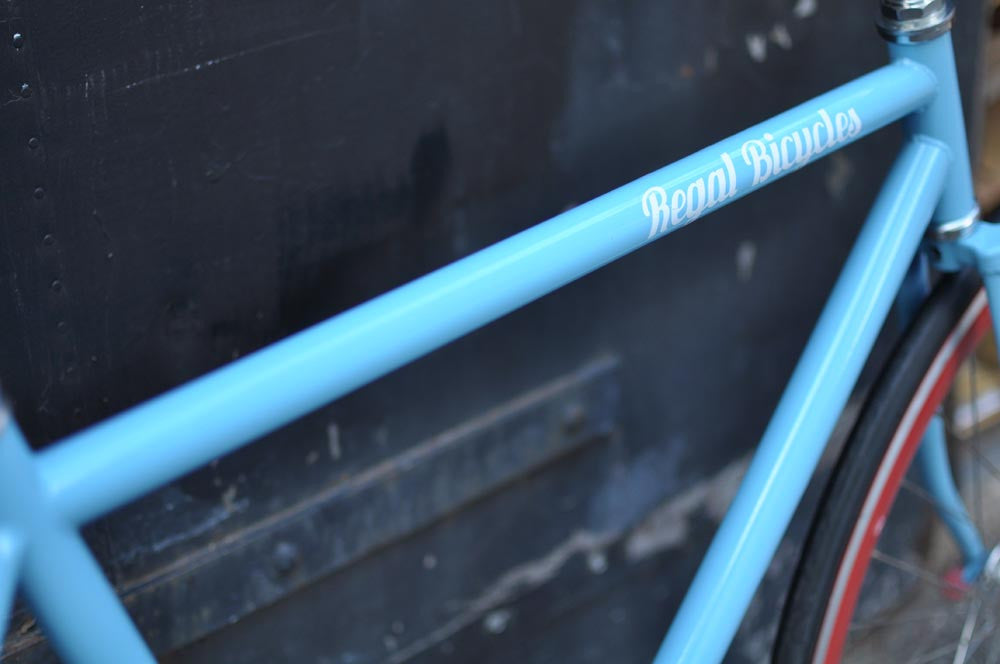 This fixed gear bicycle is called "The Maquis" and features red rims and a sky blue frame.