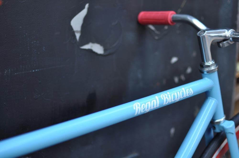 This fixed gear bicycle is called "The Maquis" and features red rims and a sky blue frame.